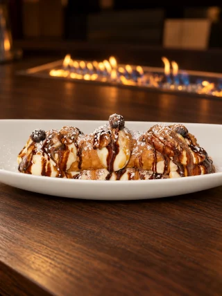 Cannoli with cream filling, powdered sugar and chocolate and caramel drizzle on a white oval dish.