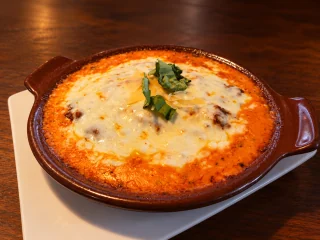 Lasagna under melted cheese and basil in a brown handled baking dish.